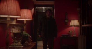 Movie still from “Men” (2022), directed by Alex Garland – A man standing in a room with a lamp on the wall; Medium shot, Over the shoulder angle
