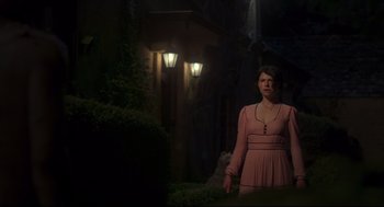 Movie still from “Men” (2022), directed by Alex Garland – A woman in a pink dress standing in the dark; Medium shot, Low angle