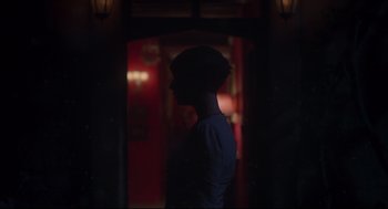 Movie still from “Men” (2022), directed by Alex Garland – A woman standing in the dark in front of a door; Medium shot, Over the shoulder angle