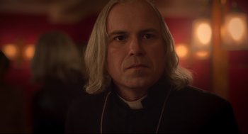 Movie still from “Men” (2022), directed by Alex Garland – A man with long blonde hair wearing a priest's outfit; Close Up shot, Over the shoulder angle