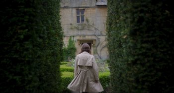 Movie still from “Men” (2022), directed by Alex Garland – A woman in a trench coat walking through a garden; Wide shot, Over the shoulder angle