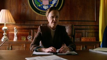 Movie still from “Narcos” (2015), created by Chris Brancato – A woman sitting at a desk in front of papers; Medium shot, Low angle