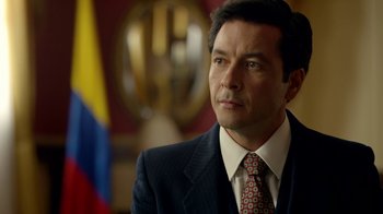 Movie still from “Narcos” (2015), created by Chris Brancato – A person wearing a suit and tie; Close Up shot, Over the shoulder angle