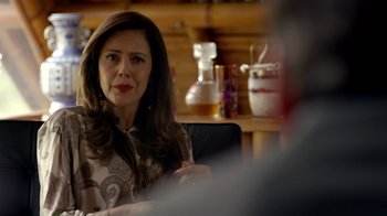 Movie still from “Narcos” (2015), created by Chris Brancato – A woman sitting in front of a man in front of a wooden table; Close Up shot, Over the shoulder angle