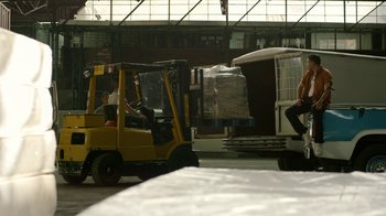 Movie still from “Narcos” (2015), created by Chris Brancato – Two men driving a yellow forklift in an industrial setting; Wide shot, Low angle