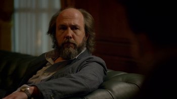 Movie still from “Narcos” (2015), created by Chris Brancato – A man sitting on a chair with a beard; Close Up shot, Over the shoulder angle