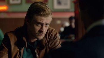 Movie still from “Narcos” (2015), created by Chris Brancato – A person sitting in a room; Close Up shot, Over the shoulder angle