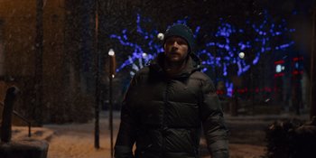 Movie still from “Midsommar” (2019), directed by Ari Aster – A man wearing a black jacket and a blue hat is standing in the snow; Medium shot, Over the shoulder angle