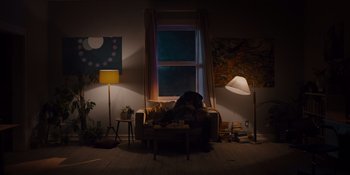 Movie still from “Midsommar” (2019), directed by Ari Aster – A person sitting on a couch in a living room; Extreme Wide shot, Low angle