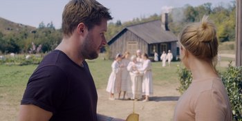 Movie still from “Midsommar” (2019), directed by Ari Aster – A man holding a piece of bread in front of a group of people; Medium shot, Over the shoulder angle
