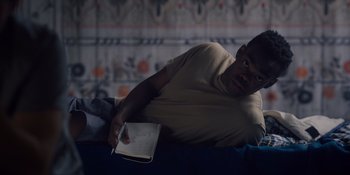 Movie still from “Midsommar” (2019), directed by Ari Aster – A man sitting on a bed holding a notebook; Medium shot, Overhead angle