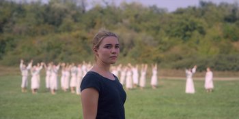 Movie still from “Midsommar” (2019), directed by Ari Aster – A woman standing in front of a group of people in a field; Medium shot, Over the shoulder angle