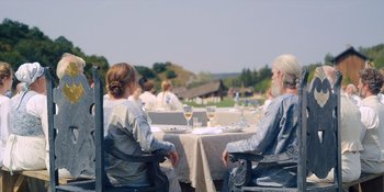 Movie still from “Midsommar” (2019), directed by Ari Aster – A group of people sitting at a table with wine glasses; Wide shot, Over the shoulder angle