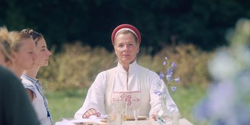 Movie still from “Midsommar” (2019), directed by Ari Aster – A woman sitting at a table with a plate of food in front of her; Medium shot, Low angle