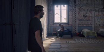 Movie still from “Midsommar” (2019), directed by Ari Aster – A man standing in front of another man sitting on a bed in front of a window; Wide shot, High angle