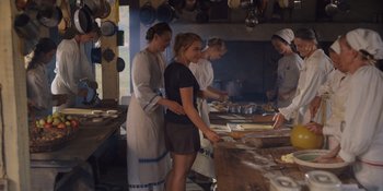 Movie still from “Midsommar” (2019), directed by Ari Aster – A group of people in a kitchen preparing food; Medium shot, Over the shoulder angle