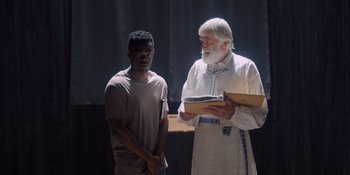 Movie still from “Midsommar” (2019), directed by Ari Aster – A man standing next to another man holding a box; Medium shot, Over the shoulder angle