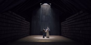 Movie still from “Midsommar” (2019), directed by Ari Aster – Two people are standing in the dark in a barn; Extreme Wide shot, Low angle
