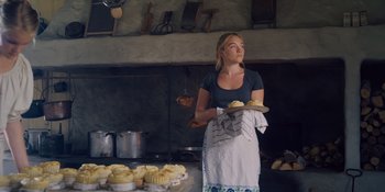 Movie still from “Midsommar” (2019), directed by Ari Aster – A woman holding a tray of food in a kitchen; Medium shot, Low angle