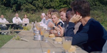 Movie still from “Midsommar” (2019), directed by Ari Aster – A group of people sitting at a table eating food; Medium shot, Over the shoulder angle