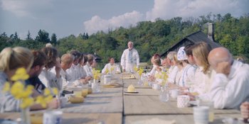 Movie still from “Midsommar” (2019), directed by Ari Aster – A group of people sitting around a table; Wide shot, Low angle