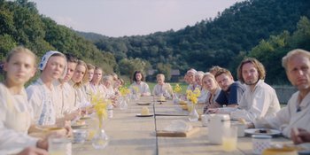 Movie still from “Midsommar” (2019), directed by Ari Aster – A group of people sitting at a long wooden table; Wide shot, High angle
