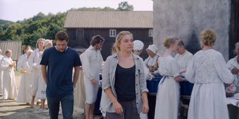 Movie still from “Midsommar” (2019), directed by Ari Aster – A group of people standing around a building; Wide shot, Over the shoulder angle
