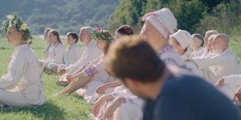Movie still from “Midsommar” (2019), directed by Ari Aster – A group of people sitting on the grass; Wide shot, Over the shoulder angle