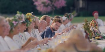 Movie still from “Midsommar” (2019), directed by Ari Aster – A group of people sitting at a long dinner table; Wide shot, Over the shoulder angle