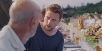 Movie still from “Midsommar” (2019), directed by Ari Aster – A young man talking to an older man at an outdoor table; Close Up shot, Over the shoulder angle