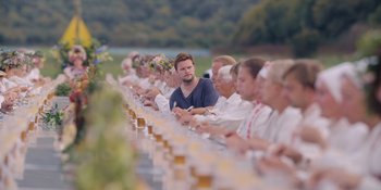 Movie still from “Midsommar” (2019), directed by Ari Aster – A group of people sitting around a long table; Wide shot, Over the shoulder angle
