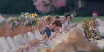Movie still from “Midsommar” (2019), directed by Ari Aster – A group of people sitting at a long dinner table; Wide shot, Low angle