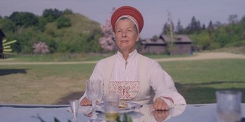 Movie still from “Midsommar” (2019), directed by Ari Aster – An older woman sitting at a table with a plate of food; Medium shot, Low angle