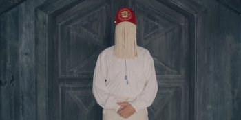 Movie still from “Midsommar” (2019), directed by Ari Aster – A man with a long white beard wearing a red hat; Close Up shot, Low angle