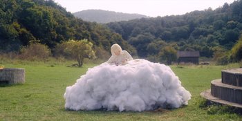 Movie still from “Midsommar” (2019), directed by Ari Aster – A woman sitting on top of a cloud in the middle of a field; Wide shot, High angle