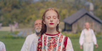 Movie still from “Midsommar” (2019), directed by Ari Aster – A young girl with red hair and eyes closed with a man behind her; Close Up shot, Over the shoulder angle