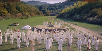 Movie still from “Midsommar” (2019), directed by Ari Aster – A large group of people in a field with trees in the background; Extreme Wide shot, High angle