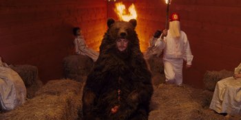 Movie still from “Midsommar” (2019), directed by Ari Aster – A man dressed as a bear sitting in front of a fire; Medium shot, Low angle
