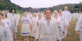 Movie still from “Midsommar” (2019), directed by Ari Aster – A group of people standing in front of each other in a field; Medium shot, Low angle