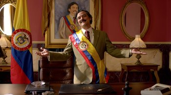 Movie still from “Narcos” (2015), created by Chris Brancato – A man in a suit with a sash around his neck; Medium shot, Low angle