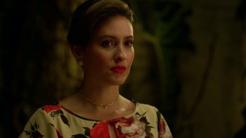 Movie still from “Narcos” (2015), created by Chris Brancato – A woman in a floral dress looking to her left; Close Up shot, Over the shoulder angle