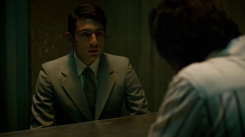 Movie still from “Narcos” (2015), created by Chris Brancato – A man wearing a suit and tie in front of a mirror; Medium shot, Over the shoulder angle