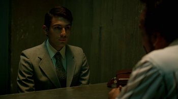 Movie still from “Narcos” (2015), created by Chris Brancato – A man sitting at a table in front of a mirror; Medium shot, Over the shoulder angle