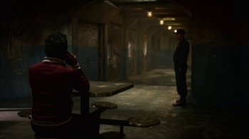 Movie still from “Narcos” (2015), created by Chris Brancato – Two men standing in a dark room next to tables and benches; Wide shot, Over the shoulder angle
