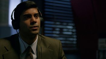 Movie still from “Narcos” (2015), created by Chris Brancato – A man in a suit and tie wearing headphones; Close Up shot, Over the shoulder angle