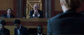 Movie still from “Miss Sloane” (2016), directed by John Madden – A man sitting in front of another man in front of a camera; Medium shot, Over the shoulder angle