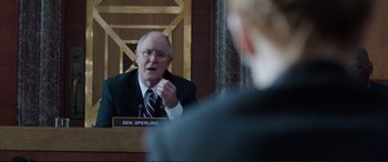 Movie still from “Miss Sloane” (2016), directed by John Madden – A man in a suit and tie sitting at a table; Medium shot, Over the shoulder angle
