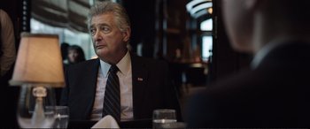 Movie still from “Miss Sloane” (2016), directed by John Madden – An older man sitting at a table in a suit; Close Up shot, Over the shoulder angle