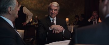 Movie still from “Miss Sloane” (2016), directed by John Madden – An older man sitting at a table in front of papers; Medium shot, Over the shoulder angle