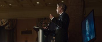 Movie still from “Miss Sloane” (2016), directed by John Madden – A man standing at a podium speaking to a crowd; Medium shot, Over the shoulder angle